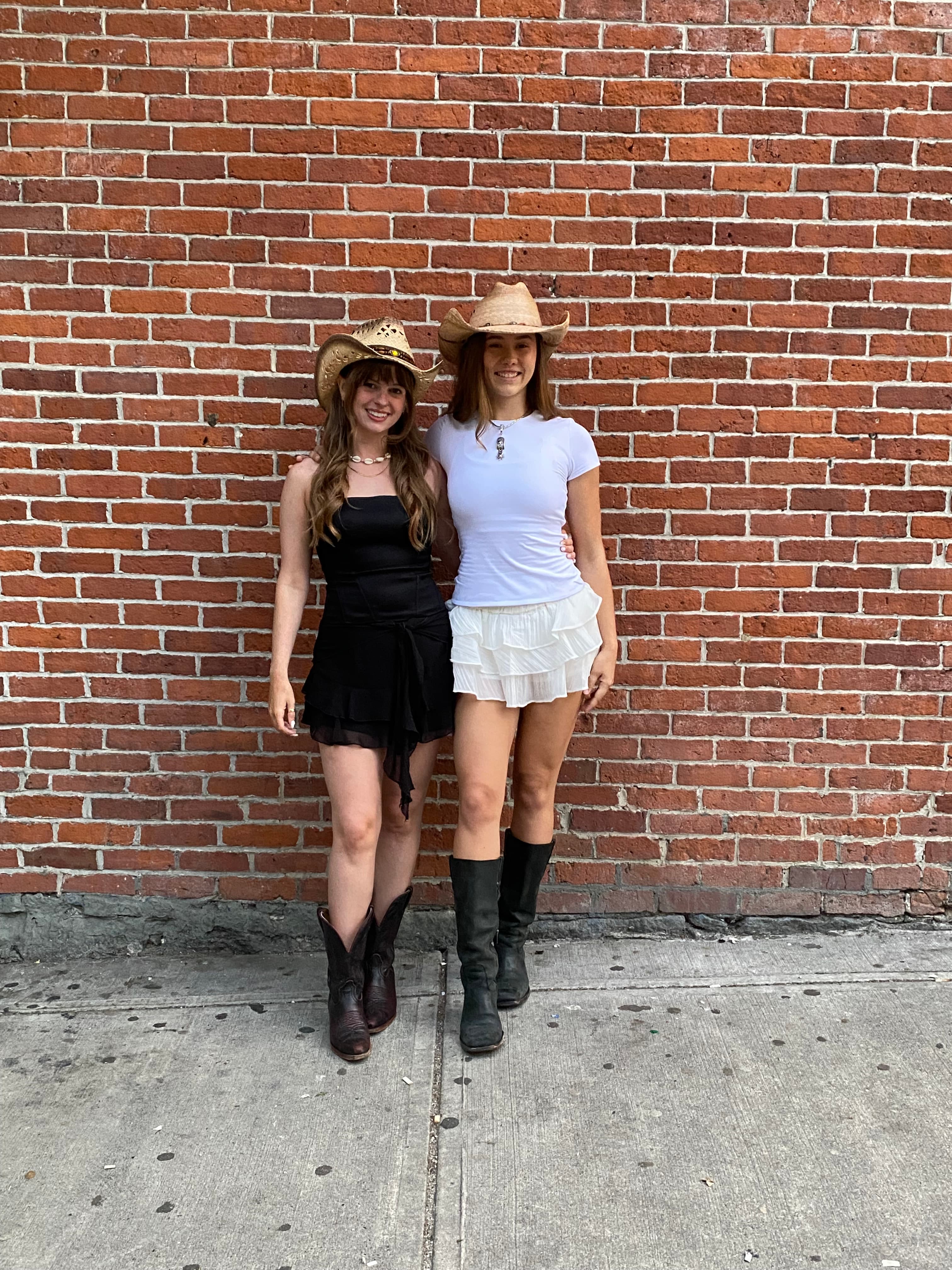 Alex and Lily of Wildflower Line Dancing in cowboy hats and boots in front of a brick wall